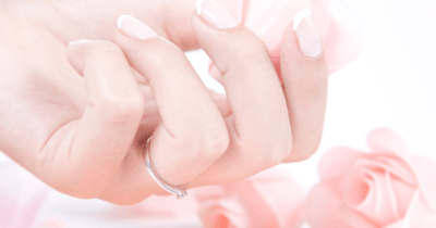 man sieht eine gepflegte Hand mit einem Fingerring. Im Hintergrund sieht man rosa Rosen. Fingerring geht als Lymph-Massage-Therapeutin nicht.