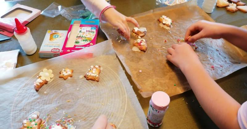 Man sieht Backpapier, auf dem Kekse zu sehen sind, die von Kinderhänden verziert werden.