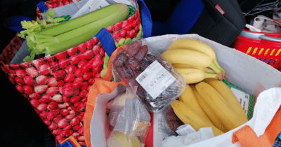 Man sieht zwei Einkaufstaschen gefüllt mit Sellerie, Bananen, Datteln usw.