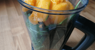 Man sieht einen Mixkrug mit Spinat, Orangensaft und Mango.
